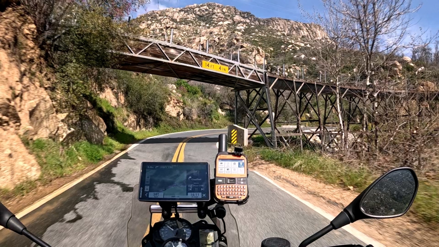 Riding along a winding mountain road, a motorcycle approaches a wooden bridge.