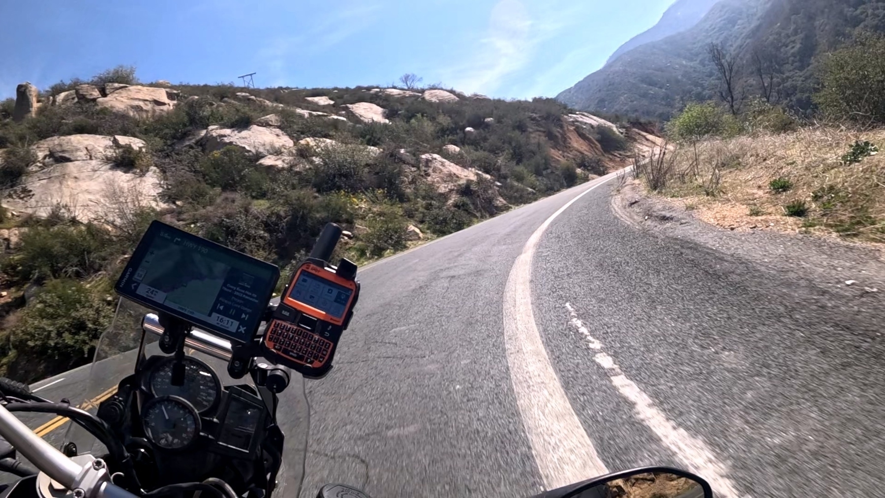 A motorcycle is traveling along a winding road through a mountainous landscape under a clear blue sky.