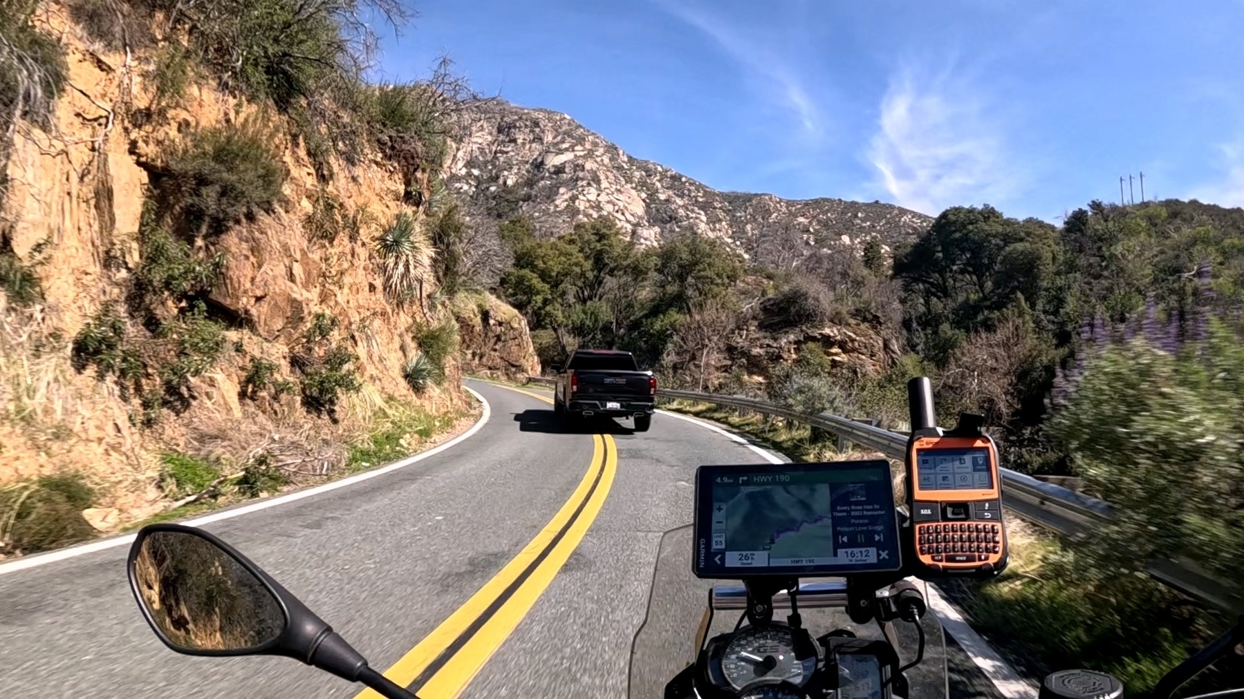 A motorcycle follows a black pickup truck on a winding mountain road.