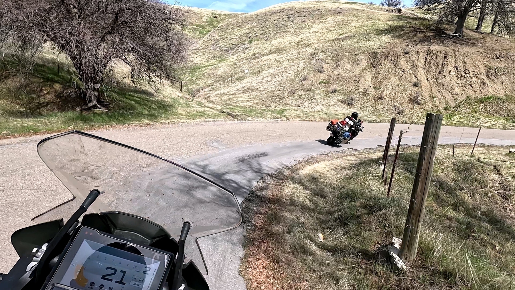 A motorcyclist is riding on a curvy rural road surrounded by grassy hills.