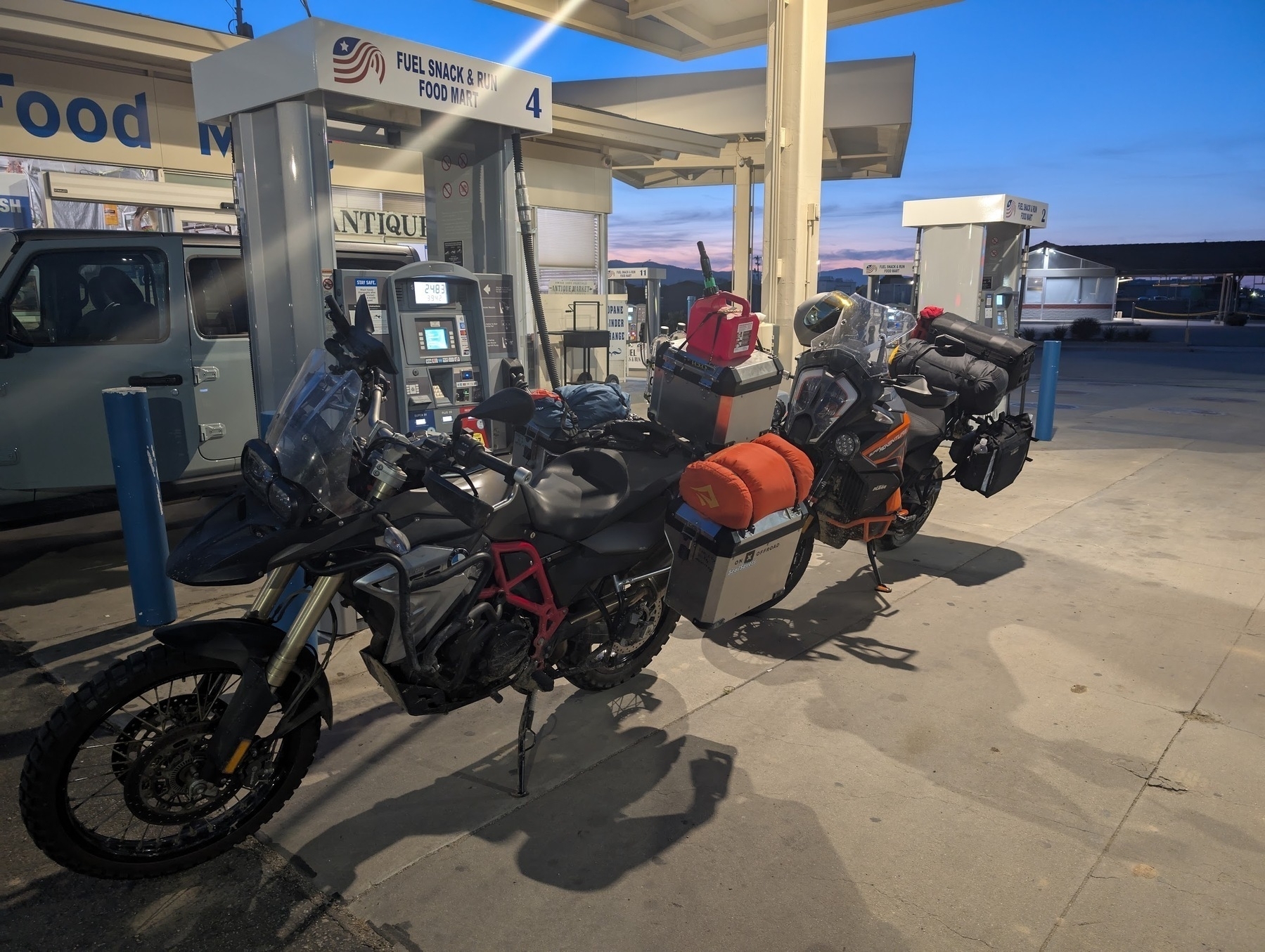 Two adventure motorcycles loaded with gear are parked at a gas station.