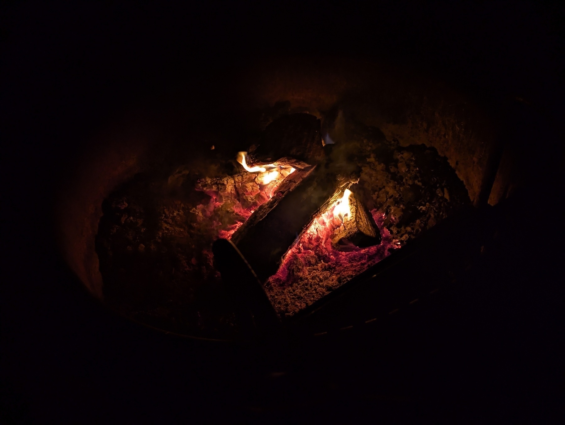 A campfire with glowing embers and partially burned logs.